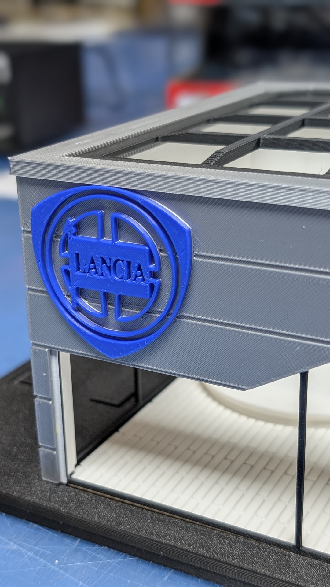 Miniatura de fachada cinzenta com logótipo azul da LANCIA
