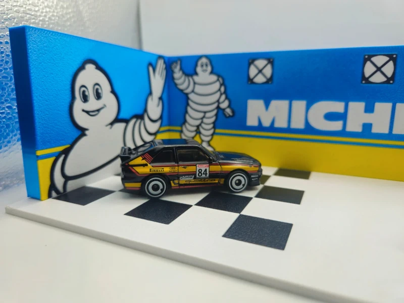Miniatura de carro de corrida preto e amarelo com número 84 e fundo decorativo Michelin