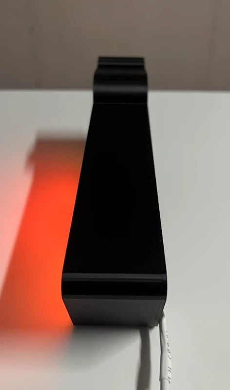 Base de suporte preta com cabo branco sobre superfície branca e sombra laranja