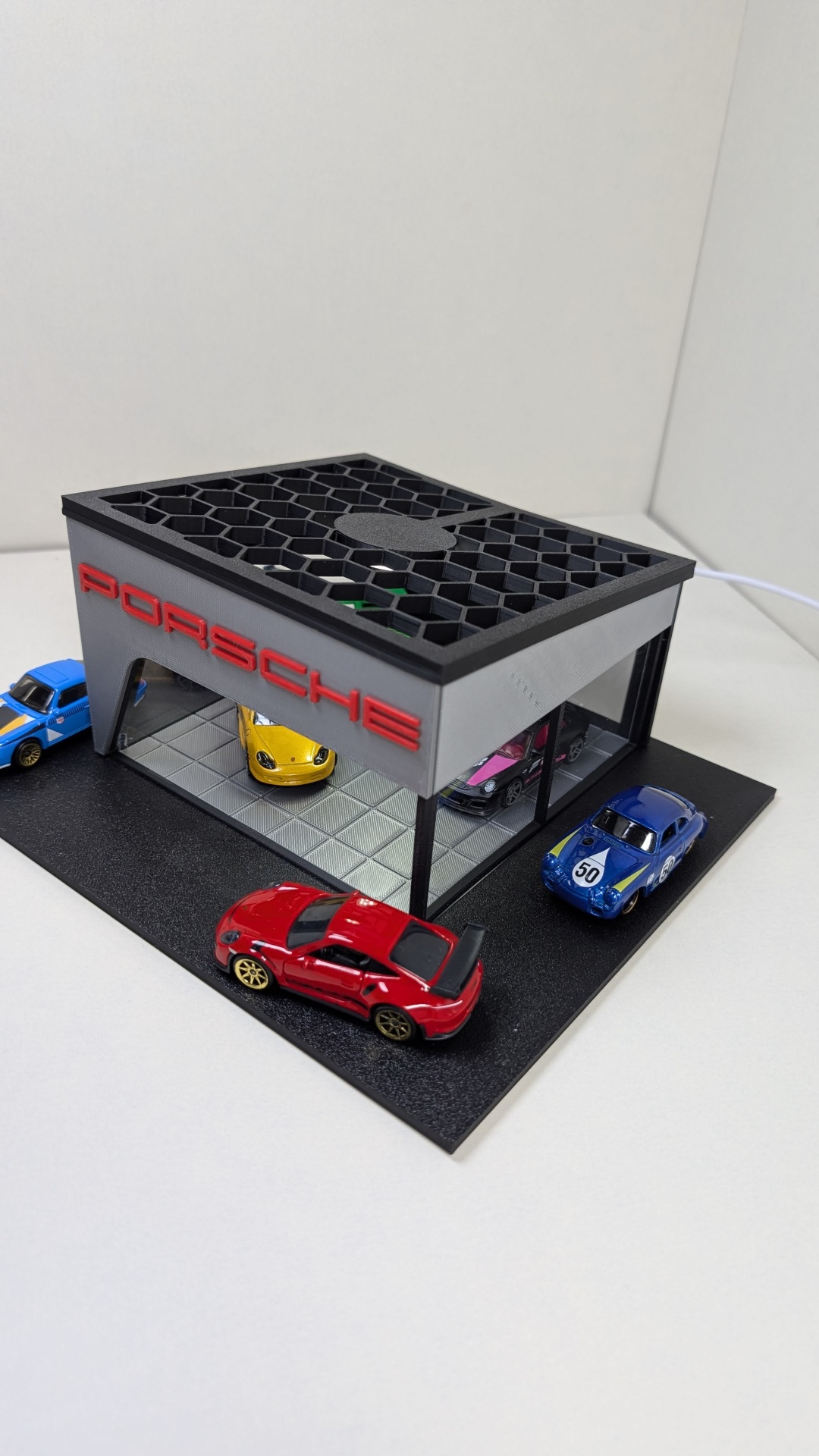 Maquete de loja Porsche com carros em miniatura à volta.
