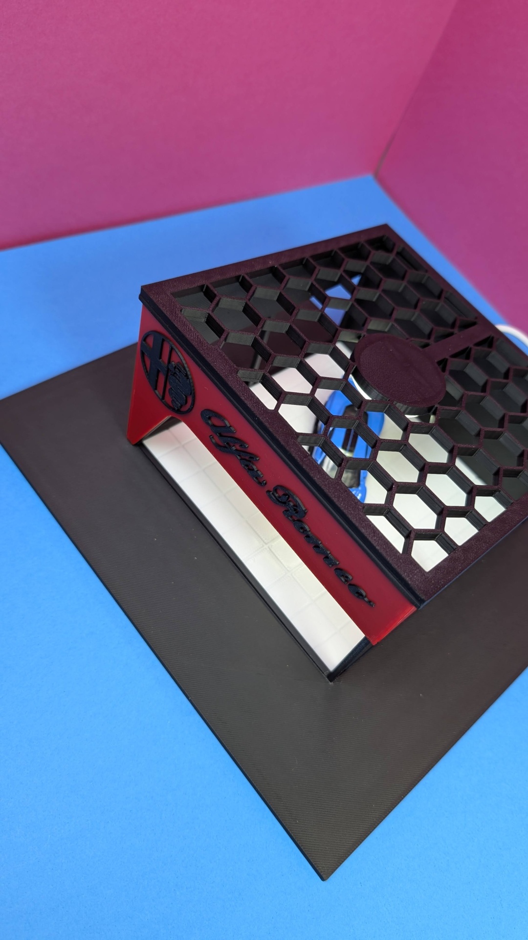 Suporte de metal vermelho e preto com padrão hexagonal e texto Alpha Ramirez