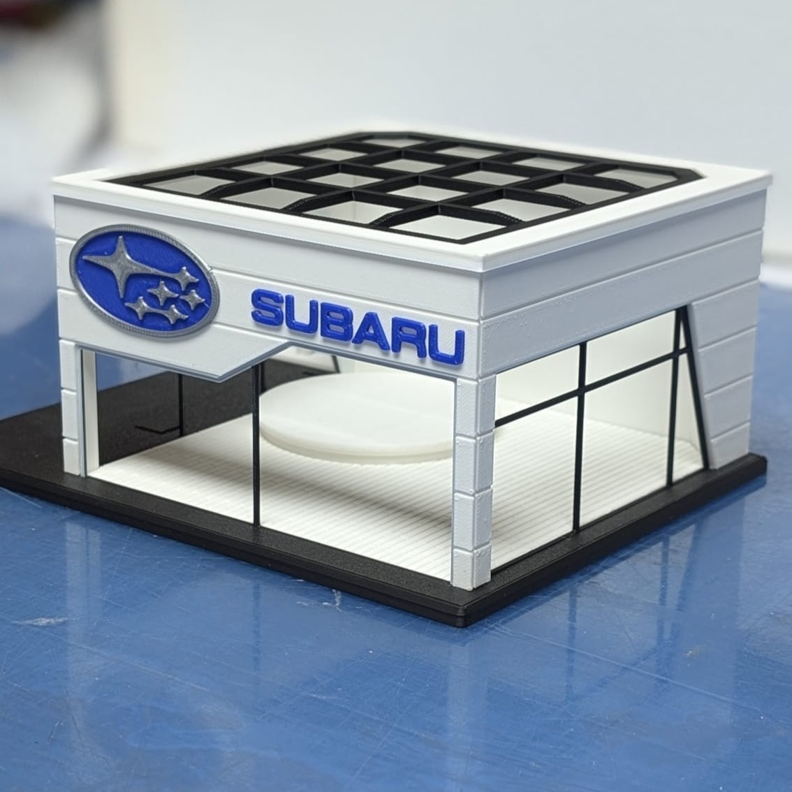Miniatura de edifício com logotipo SUBARU e estrutura branca com janelas de vidro