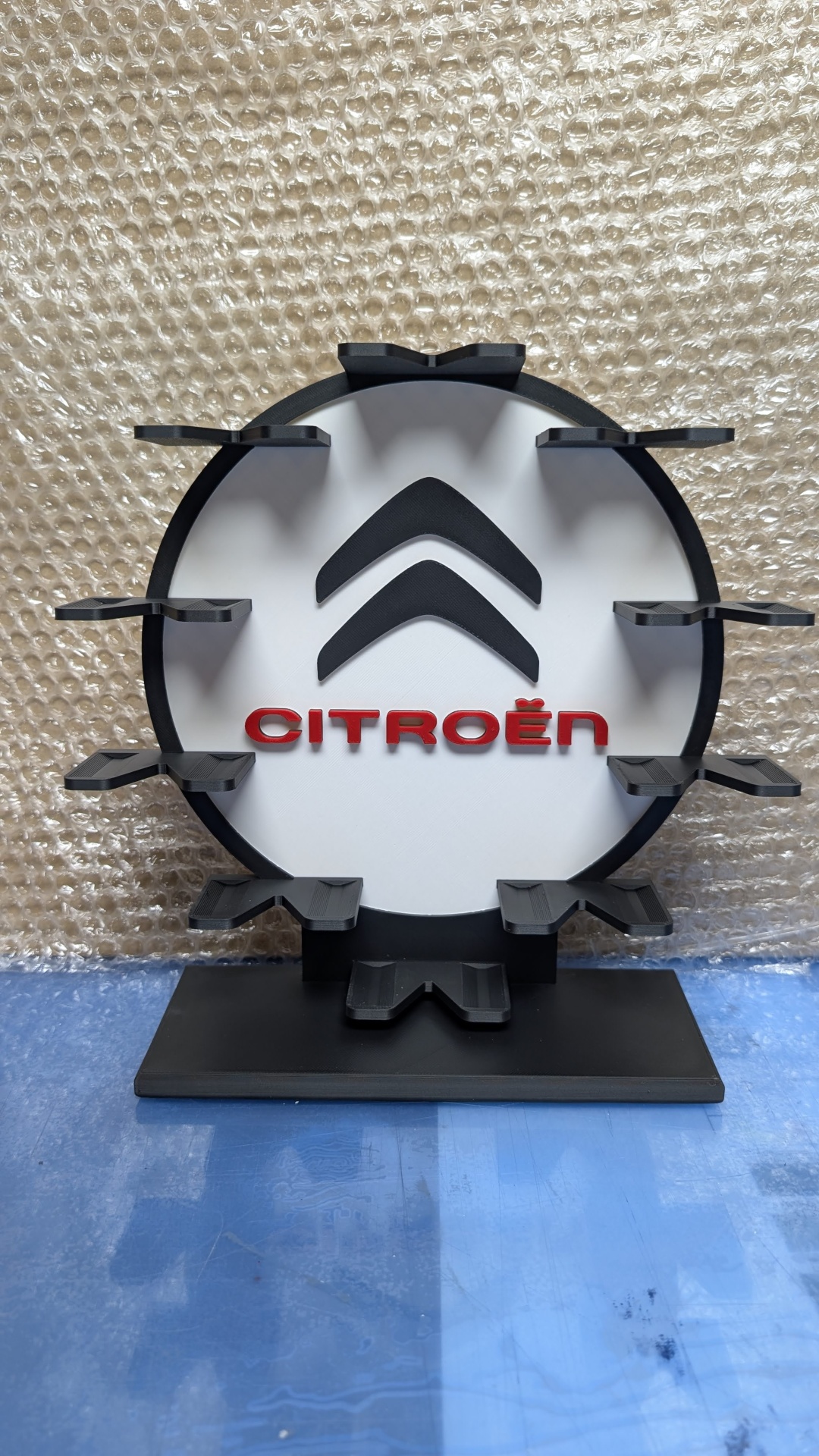Expositor redondo preto e branco com logótipo da Citroën em vermelho sobre fundo de plástico bolha.