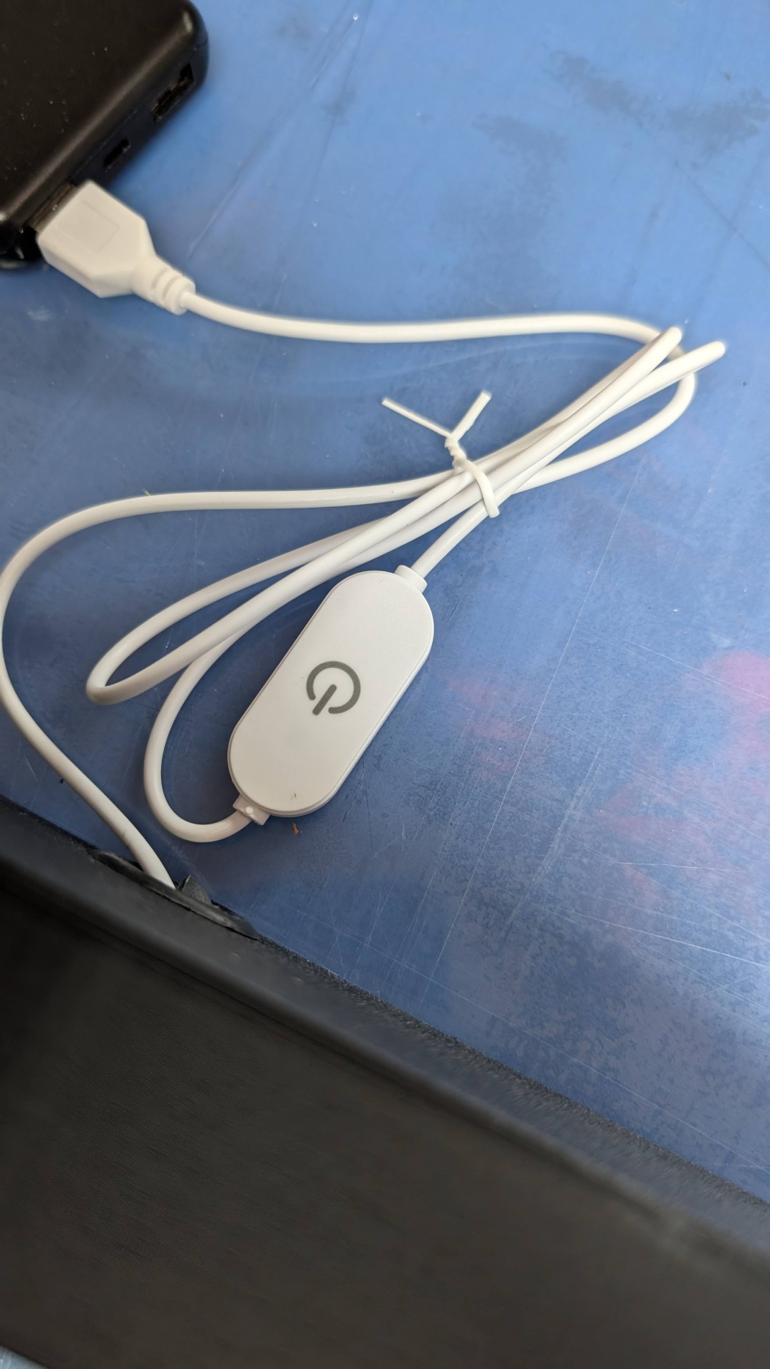 Cabo branco com interruptor ligado a dispositivo preto sobre superfície azul