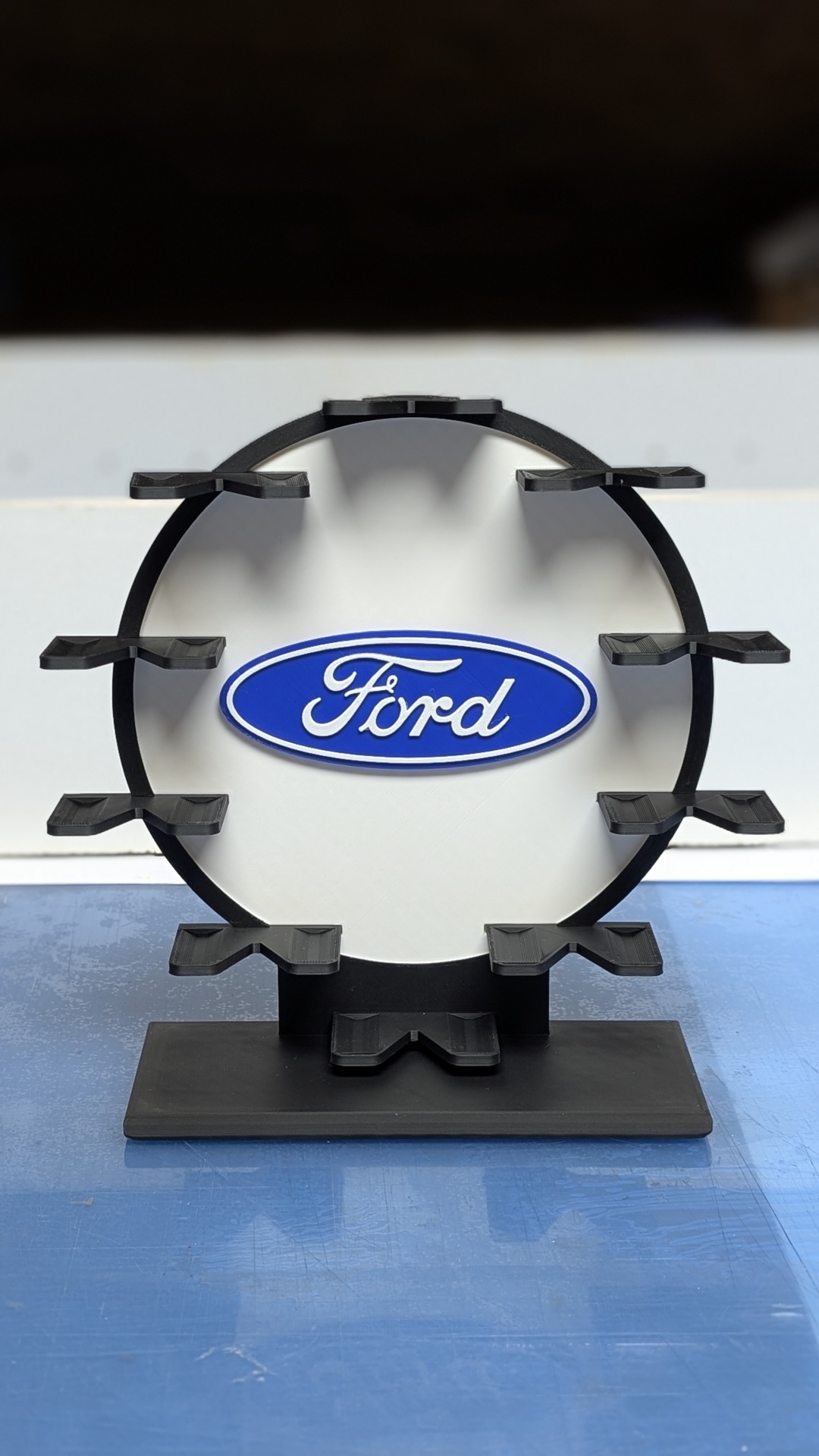 Suporte preto circular com logótipo Ford azul e branco no centro