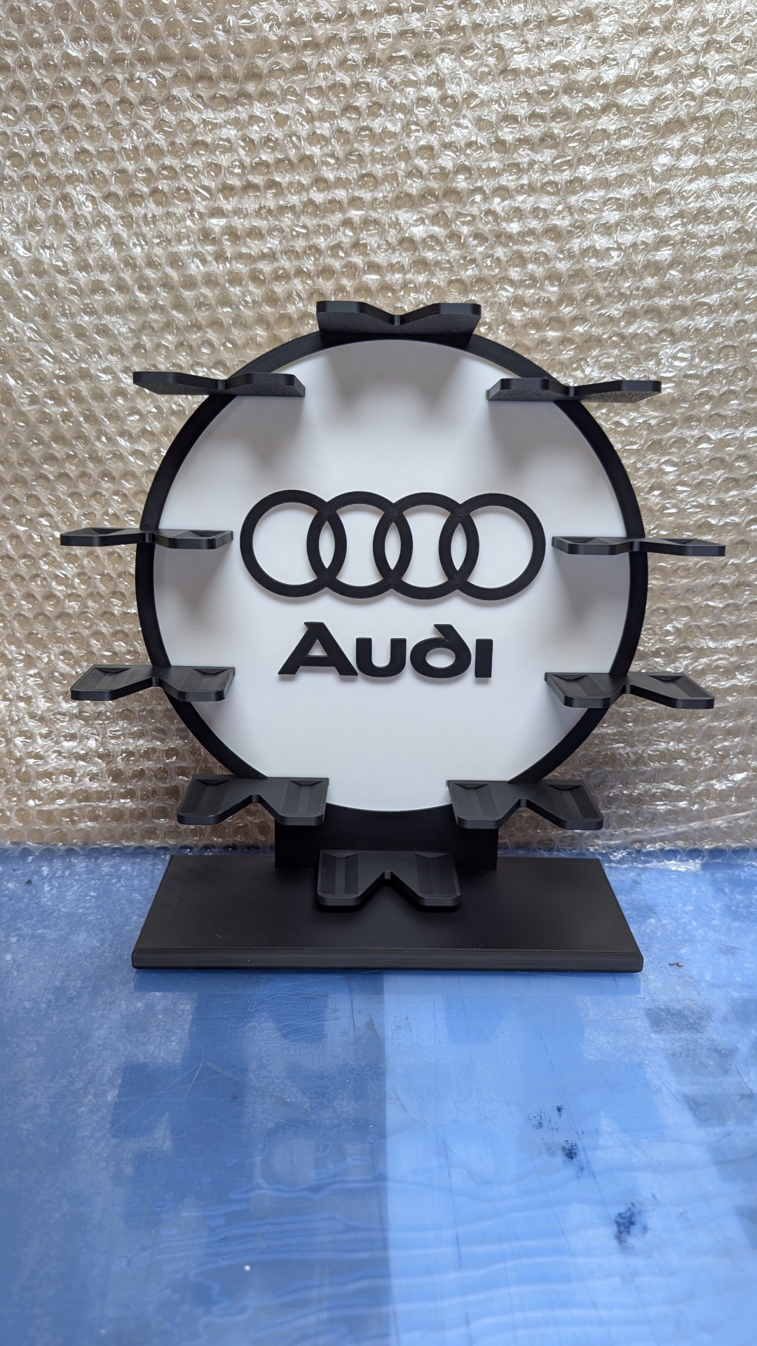 Expositor com logo da Audi em preto e branco e suportes para objetos em redor