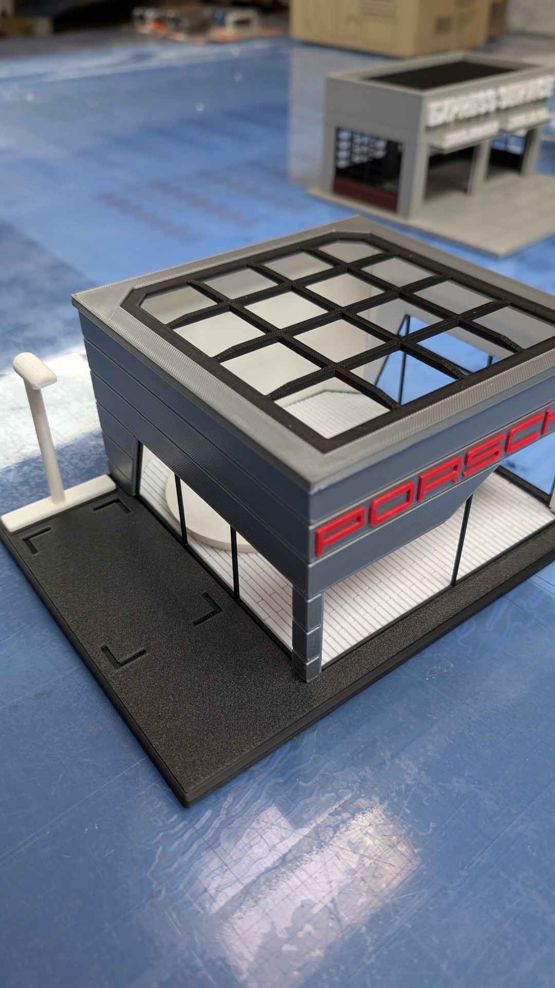 Modelo de miniatura de loja Porsche com texto vermelho numa superfície azul