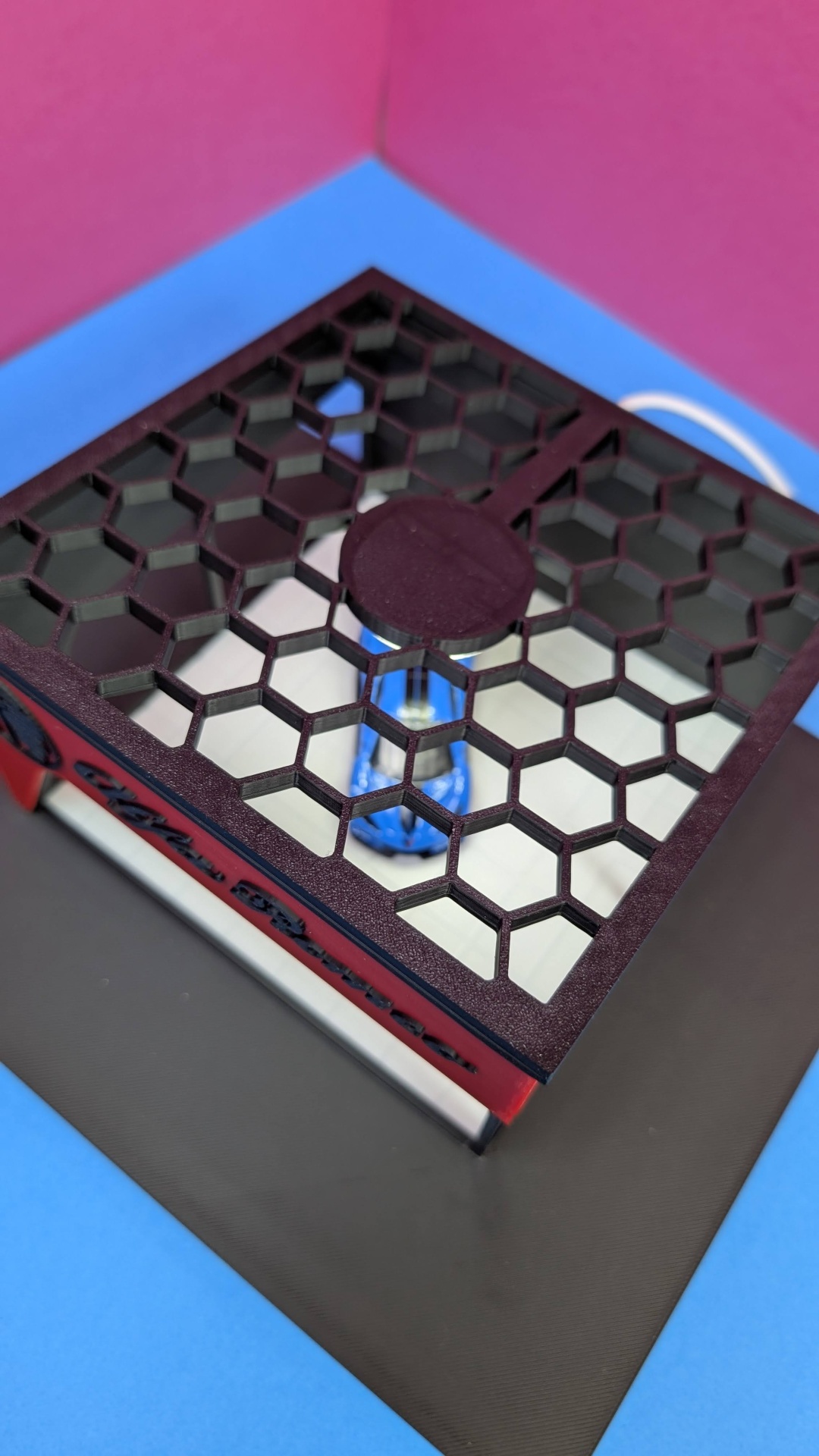 Ratoeira preta e vermelha com tampa em padrão colmeia sobre fundo azul e rosa