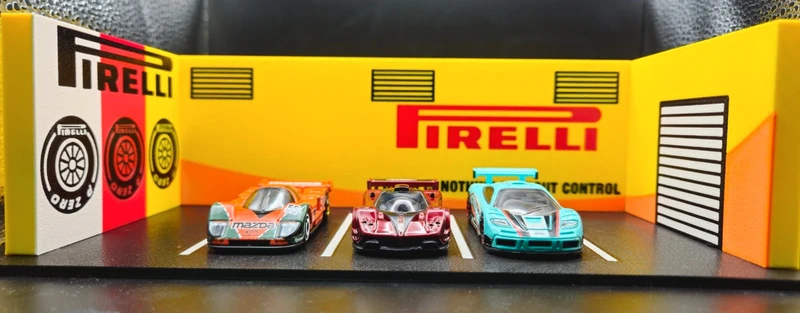 Miniaturas de carros de corrida num estacionamento de brinquedo com fundo amarelo e logo PIRELLI