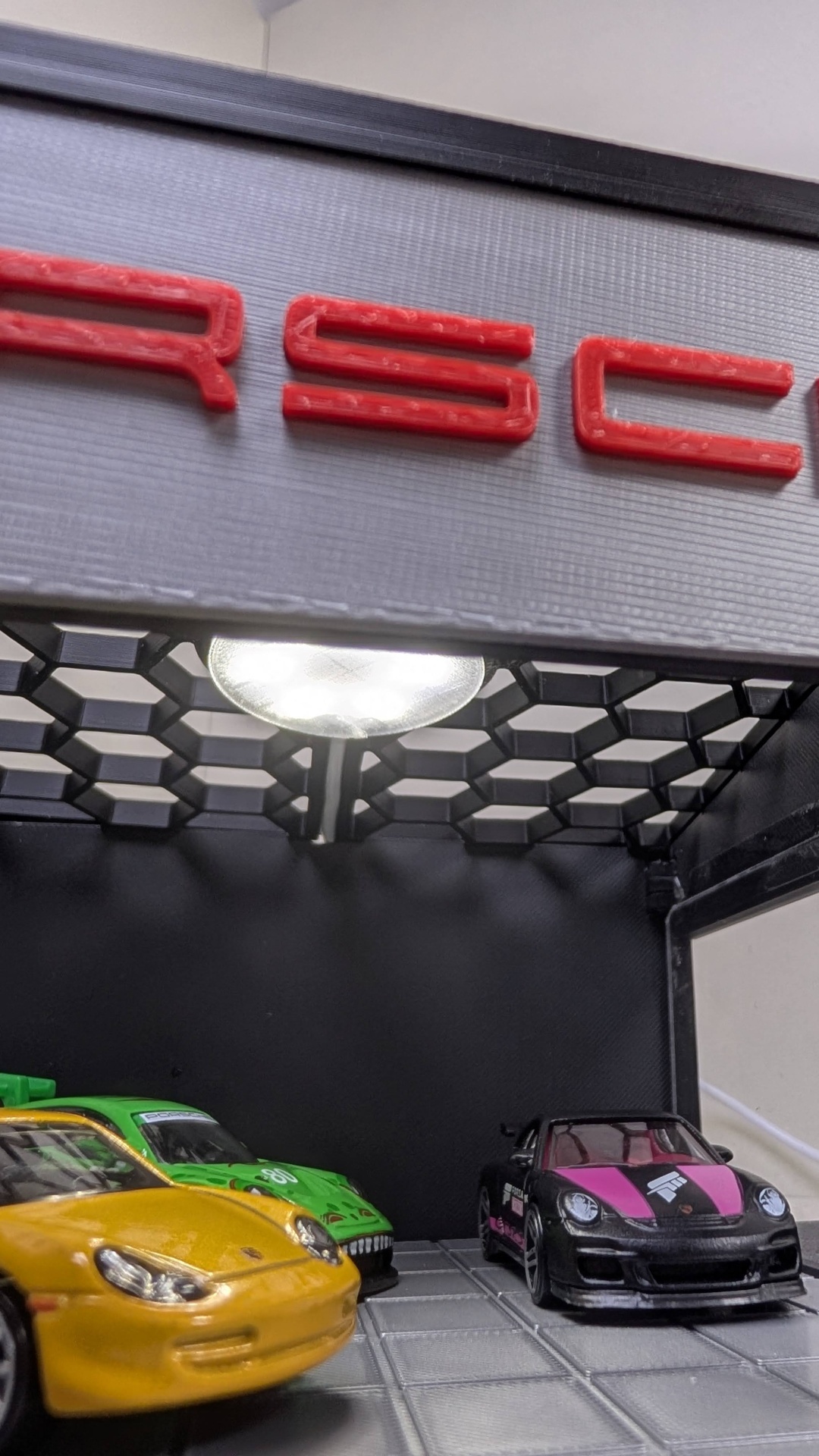 Miniaturas de carros de corrida amarelo, verde e preto num expositor com iluminação e letras vermelhas no topo