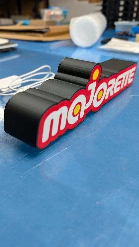 Objeto decorativo preto com a palavra majorette em detalhes vermelhos e brancos sobre superfície azul