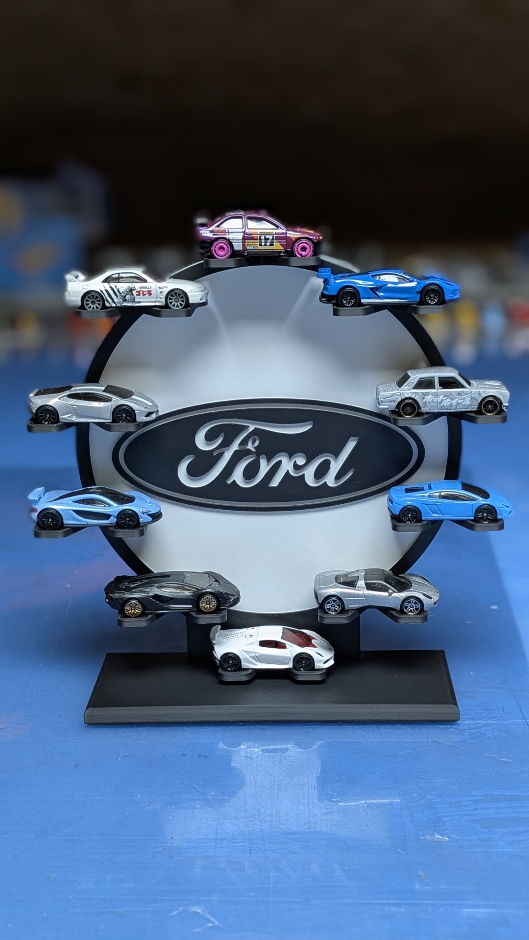Expositor circular preto e branco com logo Ford e miniaturas de carros coloridos