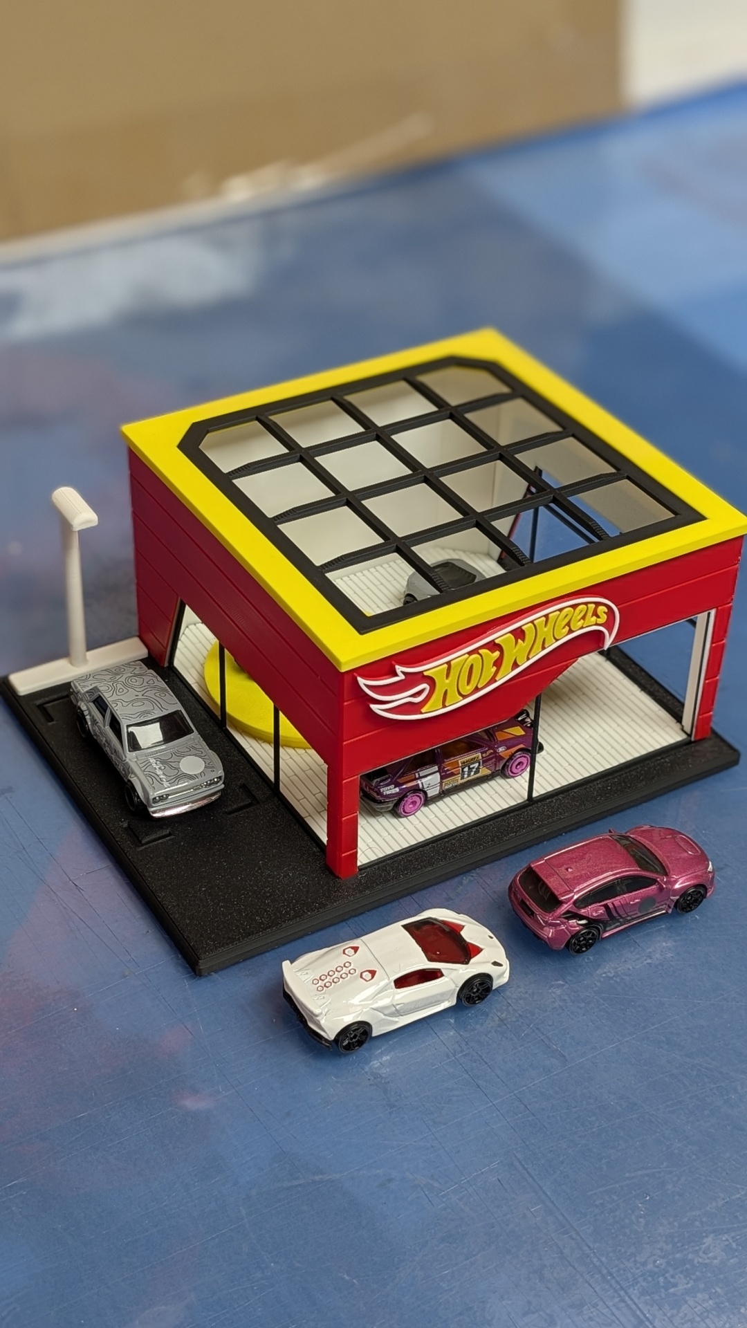 Garagem de brinquedo Hot Wheels com três carros em miniatura numa superfície azul