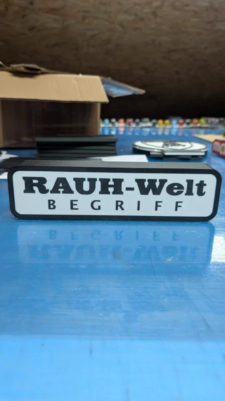 Barra decorativa com texto RAUH-Welt BEGRIFF em preto sobre fundo branco e moldura preta