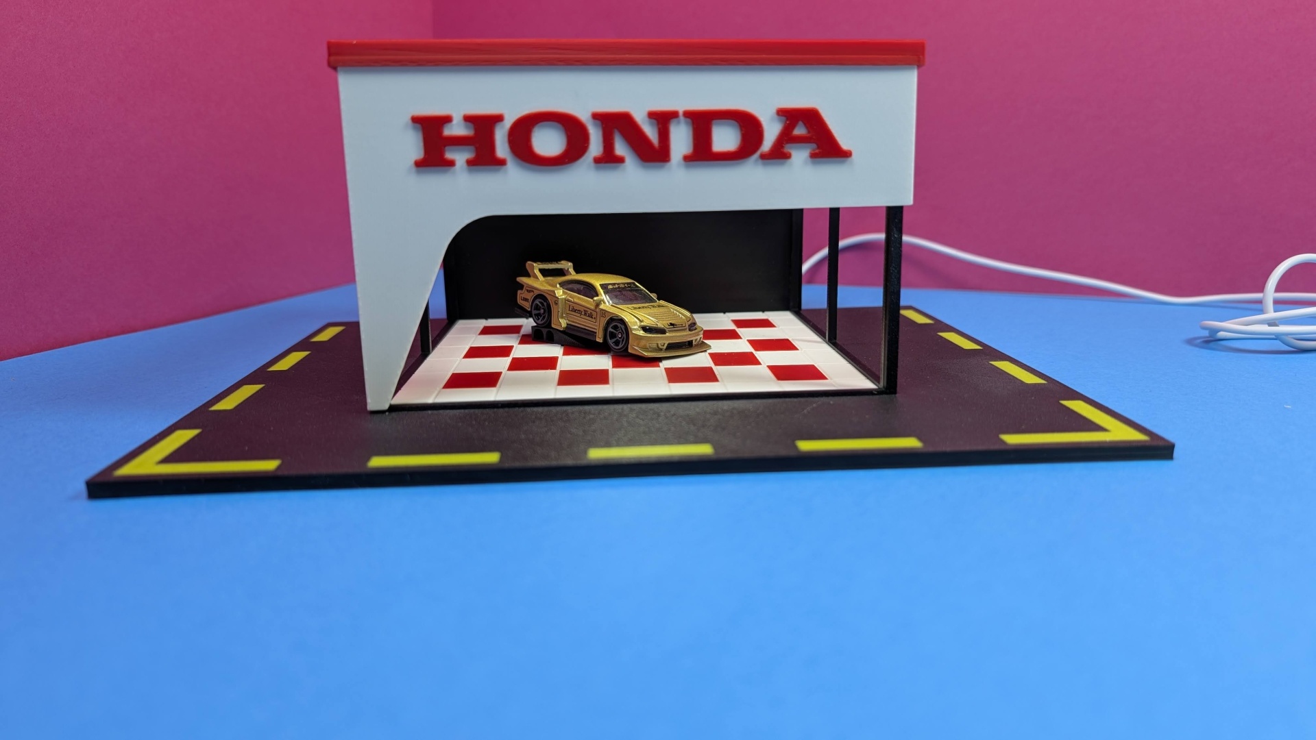 Miniatura de carro dourado numa exposição com marca Honda em vermelho