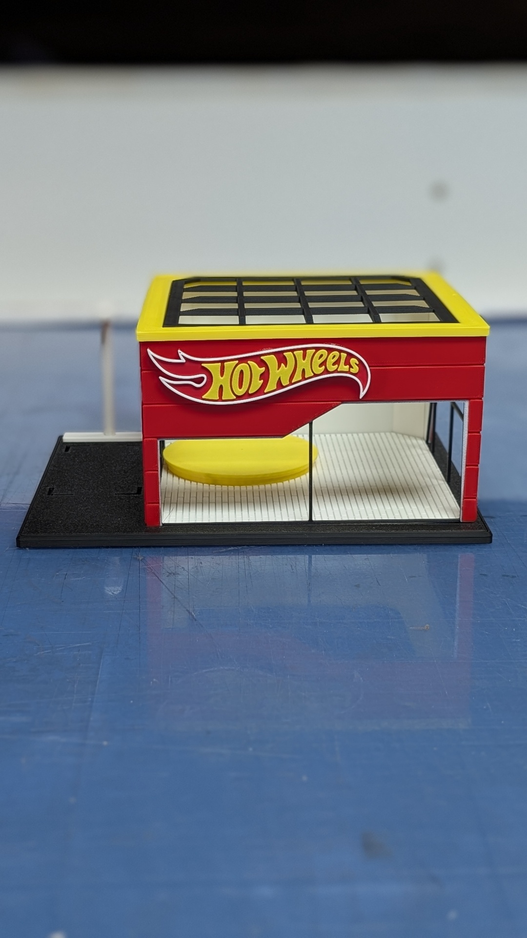 Miniatura de loja Hot Wheels em plástico vermelho, amarelo e preto com paredes de vidro