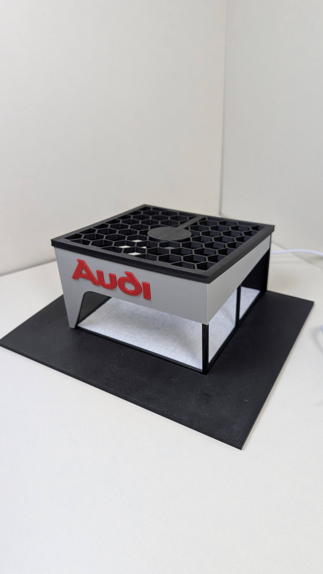Modelo 3D com logo Audi em relevo vermelho e grelha hexagonal preta no topo