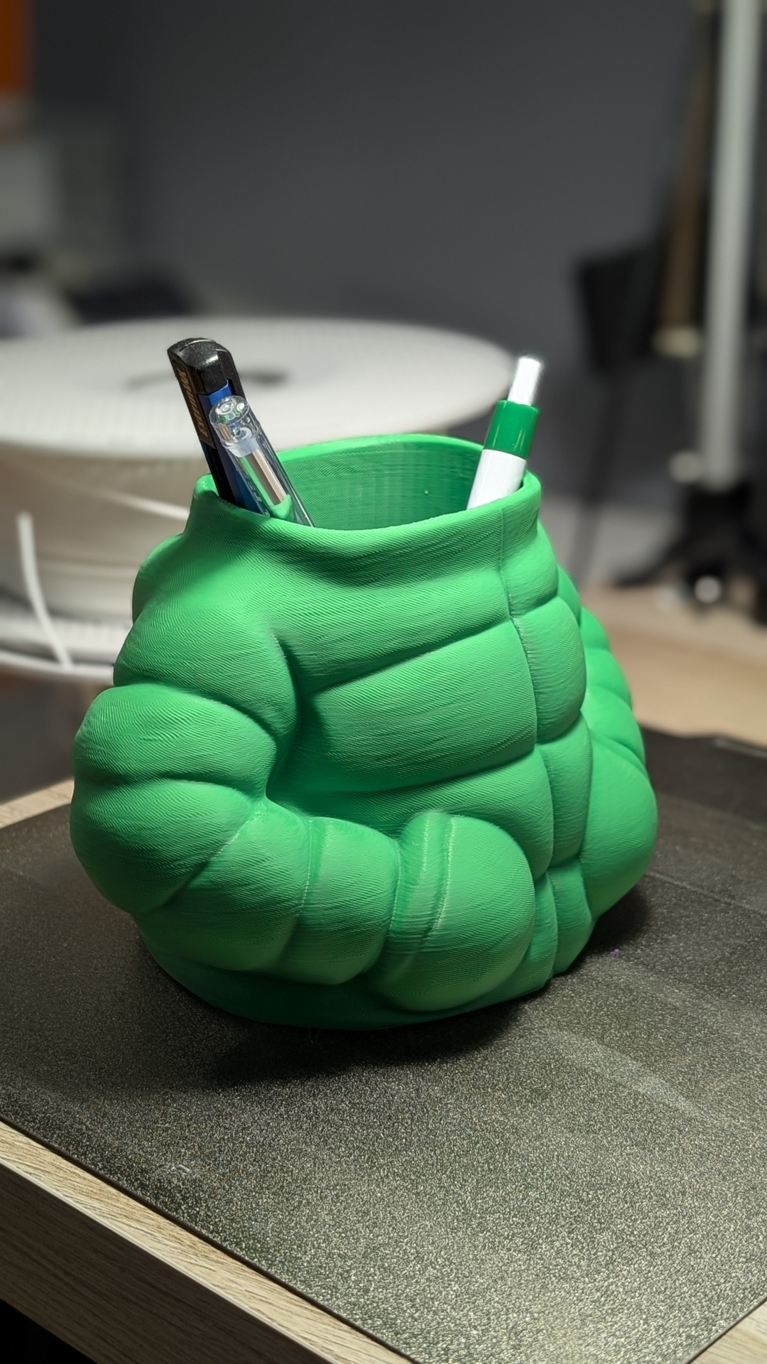 Porta-canetas verde em forma de casaco acolchoado com canetas dentro