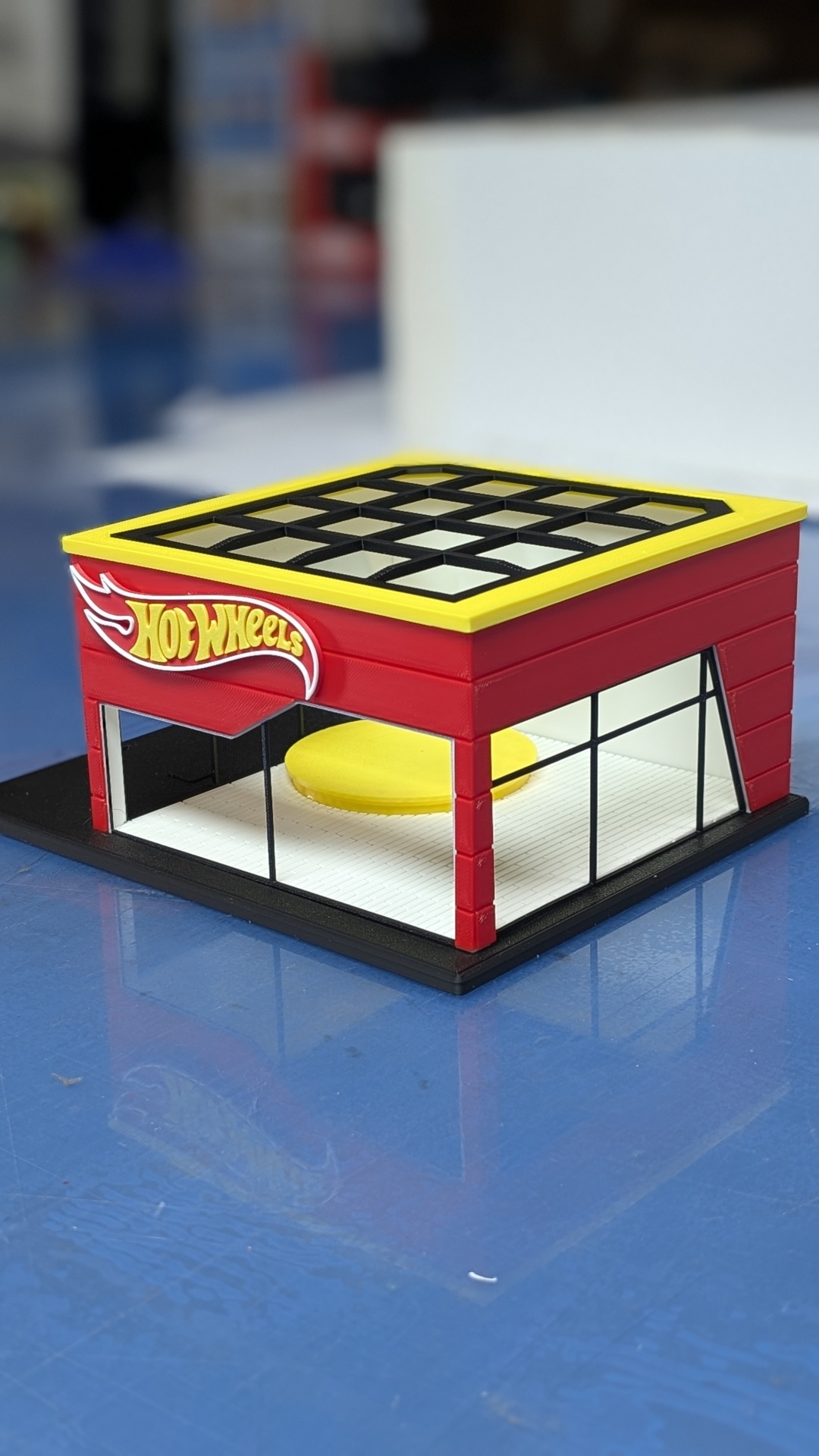 Loja miniatura Hot Wheels vermelha com teto amarelo e janelas de vidro.