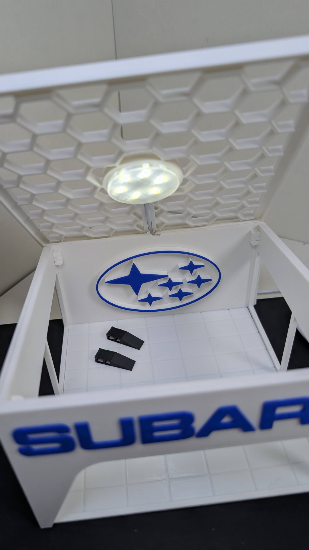 Caixa branca aberta com logo Subaru azul e luz LED no interior