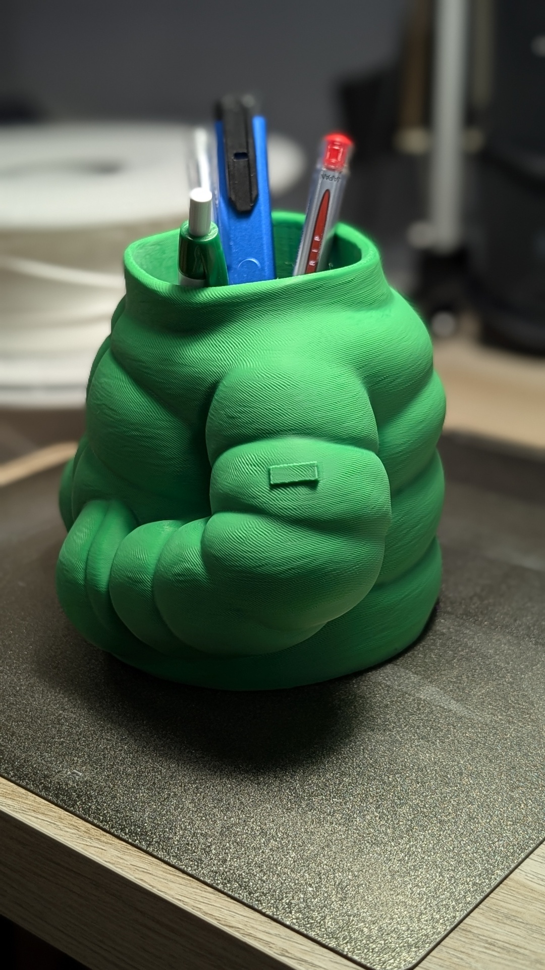 Organizador de secretária verde em forma de braço musculoso com canetas e fita adesiva