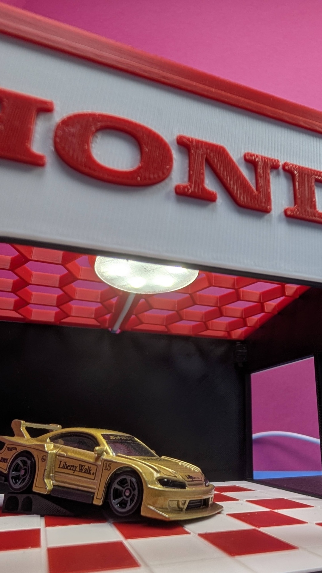 Miniatura de carro dourado com texto Liberty Walk numa base de azulejos brancos e vermelhos sob luz branca.