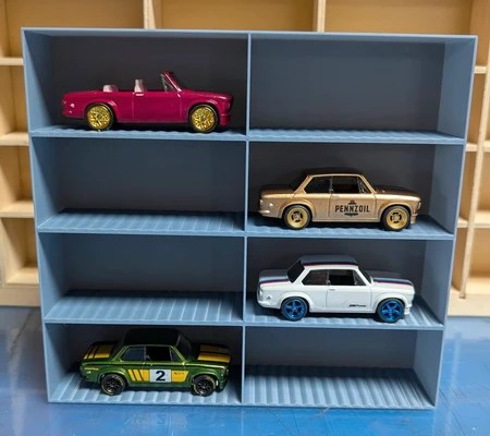 Quatro carros em miniatura em prateleira azul e fundo de madeira.