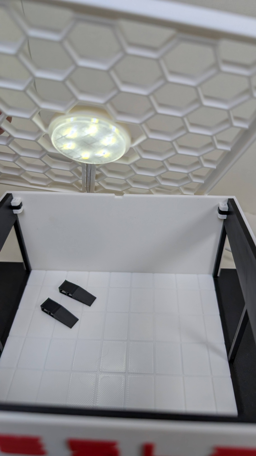 Caixa branca com interior quadrado e piso texturizado com luz LED circular acesa sobre.