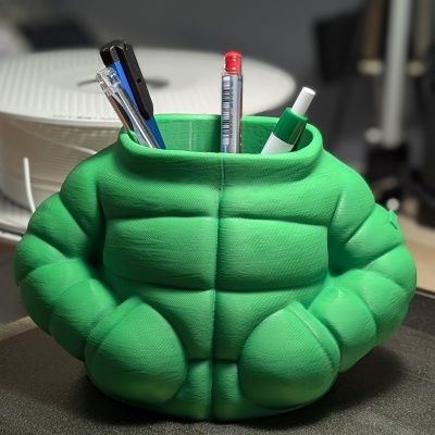 Suporte para canetas verde em forma de tronco musculado sobre mesa.