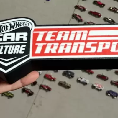 Objeto decorativo Hot Wheels com texto Team Transport e miniaturas de carros ao fundo