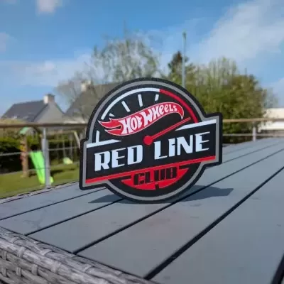 Emblema HOT WHEELS RED LINE CLUB em mesa cinza exterior com fundo de jardim