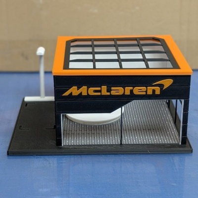 Miniatura de quiosque McLaren preto e laranja com janelas de vidro