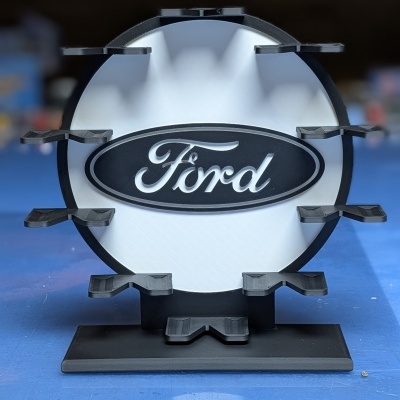 Suporte de exposição com logo Ford em branco e preto sobre base azul.