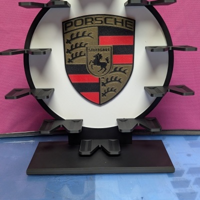 Suporte preto com logo Porsche em fundo branco e rosa.