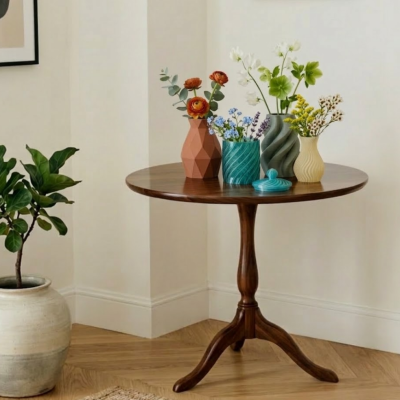 Mesa redonda de madeira com quatro vasos cerâmicos com flores artificiais e planta em vaso grande ao lado.