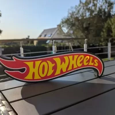 Placa decorativa Hot Wheels em madeira com texto amarelo sobre fundo vermelho em mesa exterior