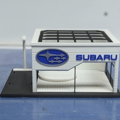 Miniatura de concessionária Subaru com logótipo e texto em azul.
