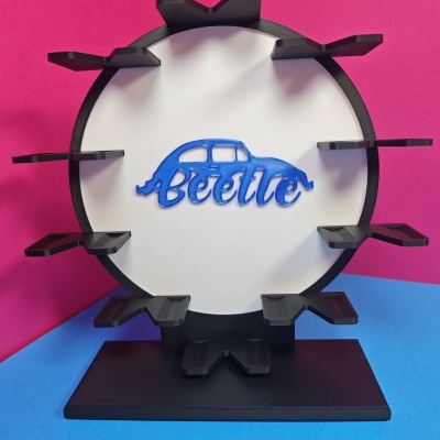 Estrutura redonda preta com painel branco e suporte para objetos, com texto Beetle azul e desenho de carrinha Beetle.