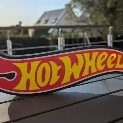Placa decorativa HOT WHEELS em plástico vermelho e amarelo numa mesa ao ar livre