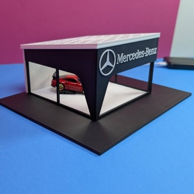 Maquete de concessionária Mercedes-Benz com carro vermelho, fundo rosa e superfície azul