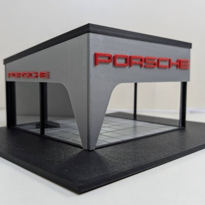 Miniatura de fachada de edifício cinzento com letras vermelhas Porsche e base preta.