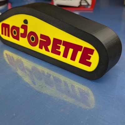 Objeto de plástico preto com face amarela e texto vermelho majorette sobre superfície azul