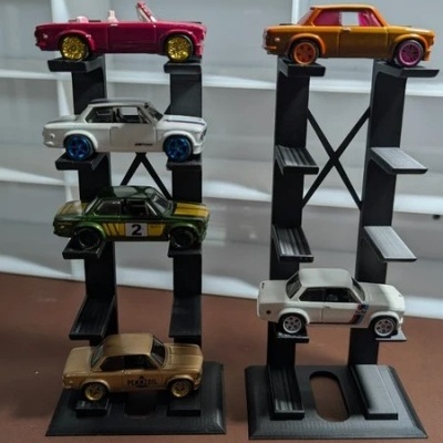 Cinco carros de brinquedo coloridos expostos em suportes pretos sobre superfície castanha