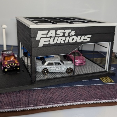 Garagem em miniatura preta com texto FAST & FURIOUS e carros em miniatura
