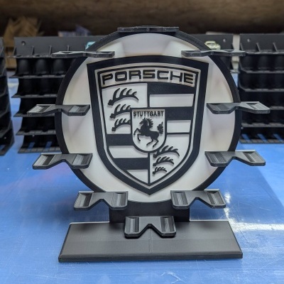 Emblema Porsche preto e branco em plástico numa superfície azul.