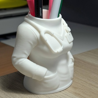 Porta-canetas branco formato torso de médico com canetas coloridas sobre mesa clara