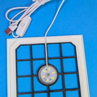 Placa quadrada branca com grelha preta, LED e cabo USB branco com interruptor