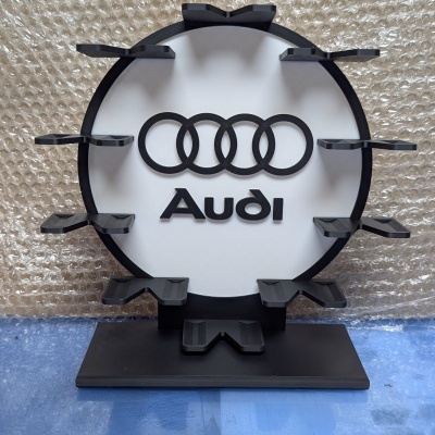 Expositor com logo da Audi em preto e branco e suportes para objetos em redor