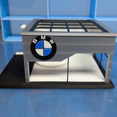 Miniatura de prédio cinzento com logótipo BMW e estante azul no fundo