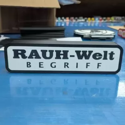 Barra decorativa com texto RAUH-Welt BEGRIFF em preto sobre fundo branco e moldura preta